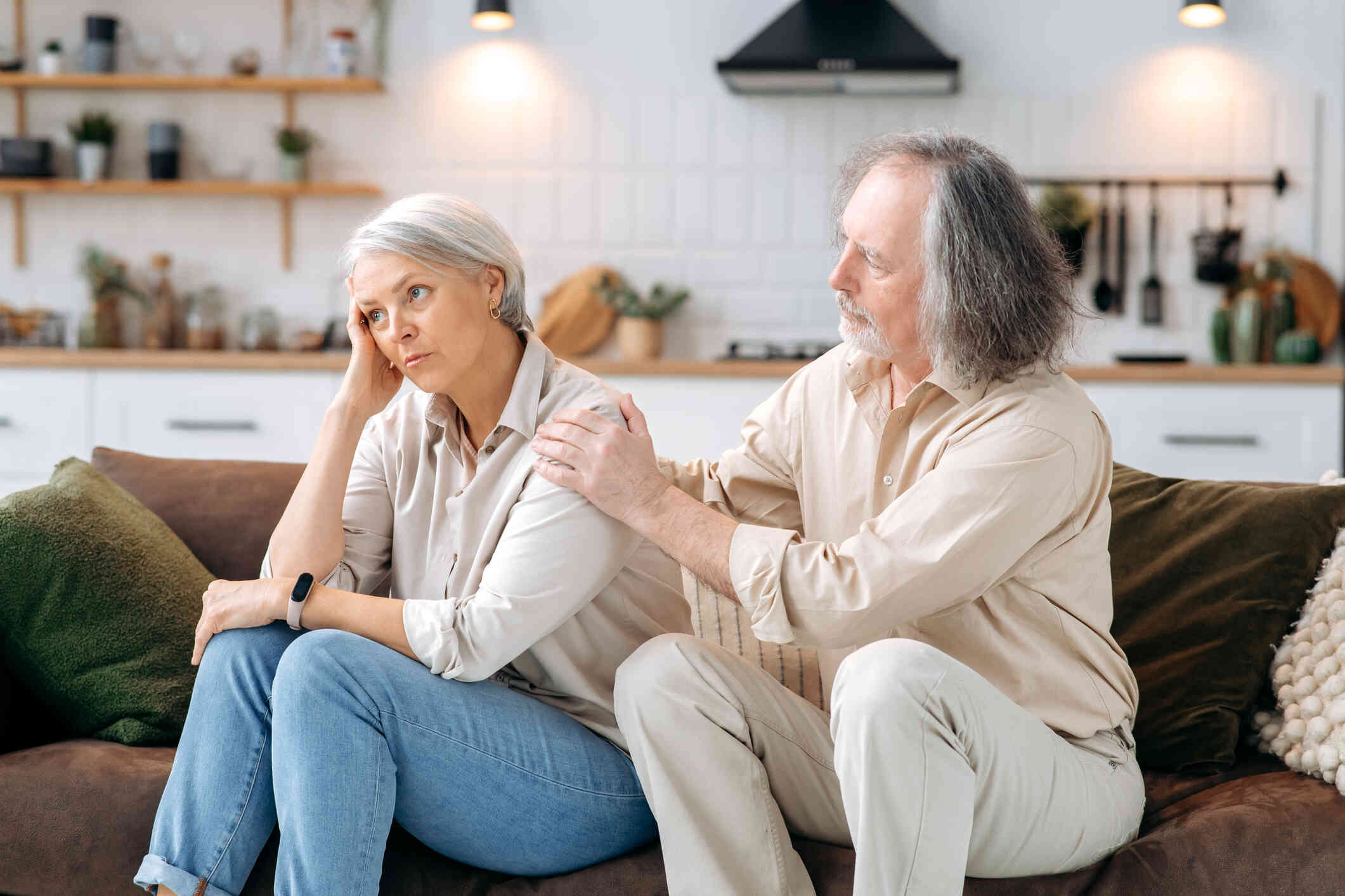 A woman turns her back on her husband as they sit in their living room as he tries to reach out and comfort her during a fight.